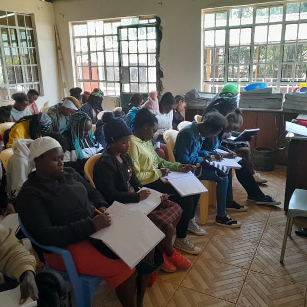 Students sitting in a classroom, focused on writing in notebooks held on their laps.